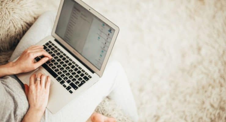 Woman on laptop sitting on fluffy rug - post regarding how to find freelance writing jobs online