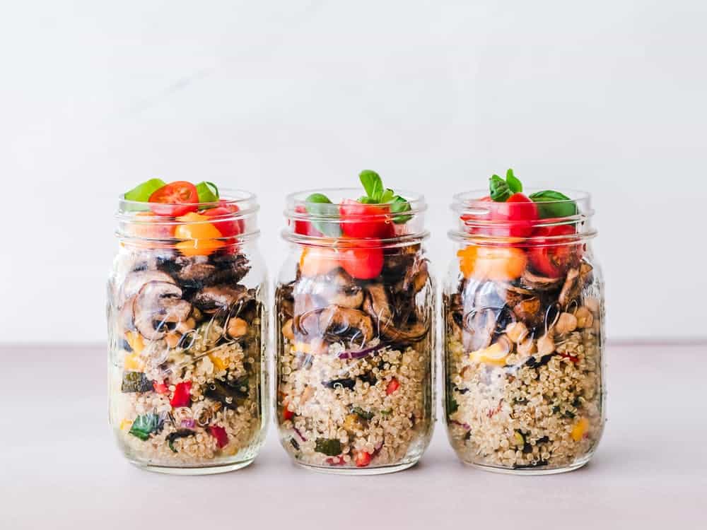 Home meal prep: three salad mason jars with layers of cous cous, mushrooms, and fresh tomatoes and basil.