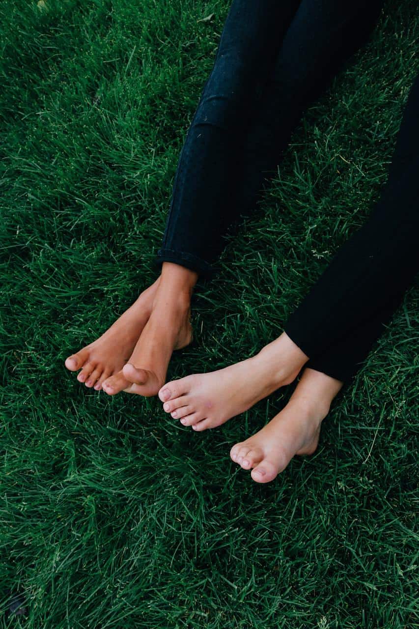 Sell feet pics: two pairs of women's feet crossed at the ankle, with a backdrop of thick grass.