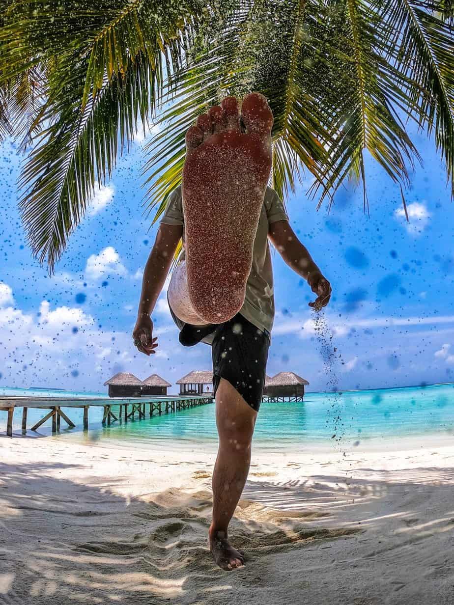 Os homens podem vender fotos de pés? Foto de um homem na praia, chutando com o pé descalço de forma que a sola do pé coberta de areia apareça para a câmera