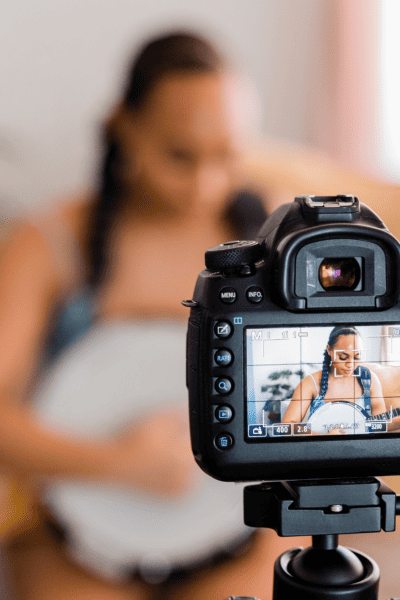 a photo of a camera filming and focusing on a person, who can be seen blurred out in the background, playing guitar.